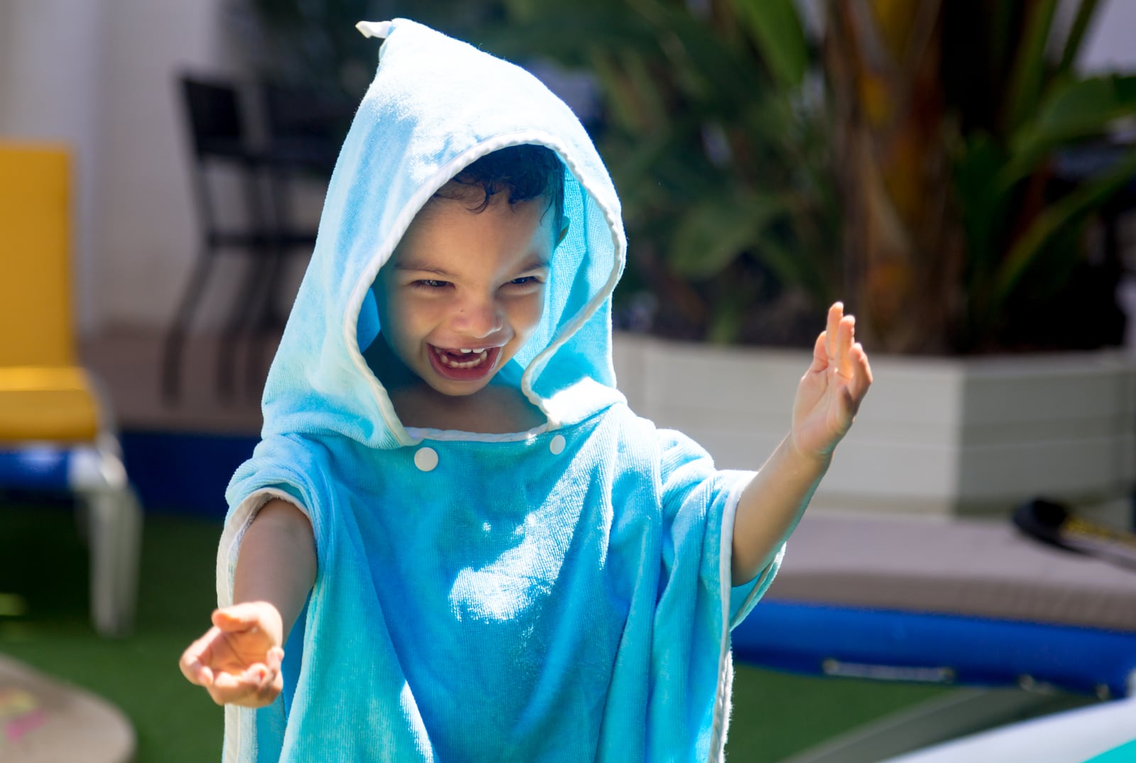 Child wearing a blue hooded towel outdoors beside a swimming pool