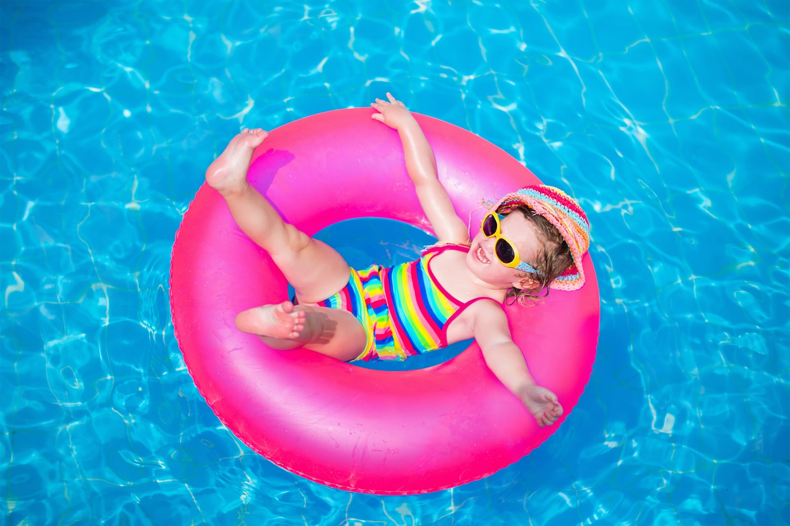 Child sitting in a bright pink inflatable ring in a swimming pool