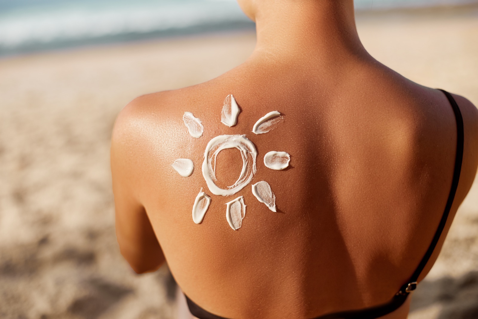 Sunscreen arranged in the shape of a sun on a person’s back at the beach